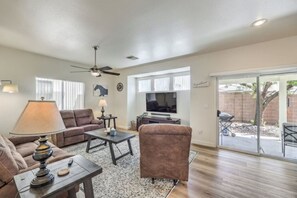 A living room with a sofa, armchair, coffee table, lamp, TV, and a sliding glass door leading to a patio.