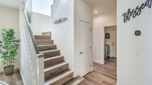 A staircase leading to a second floor, a potted plant, a wall with a 'Blessed' sign, and a laundry area. - Starling Mesa | Extended Stay Modern Vegas (North Las Vegas)