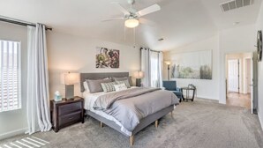 A bedroom with a bed, bedside tables, a ceiling fan, and a large window with curtains. - Starling Mesa | Extended Stay Modern Vegas (North Las Vegas)
