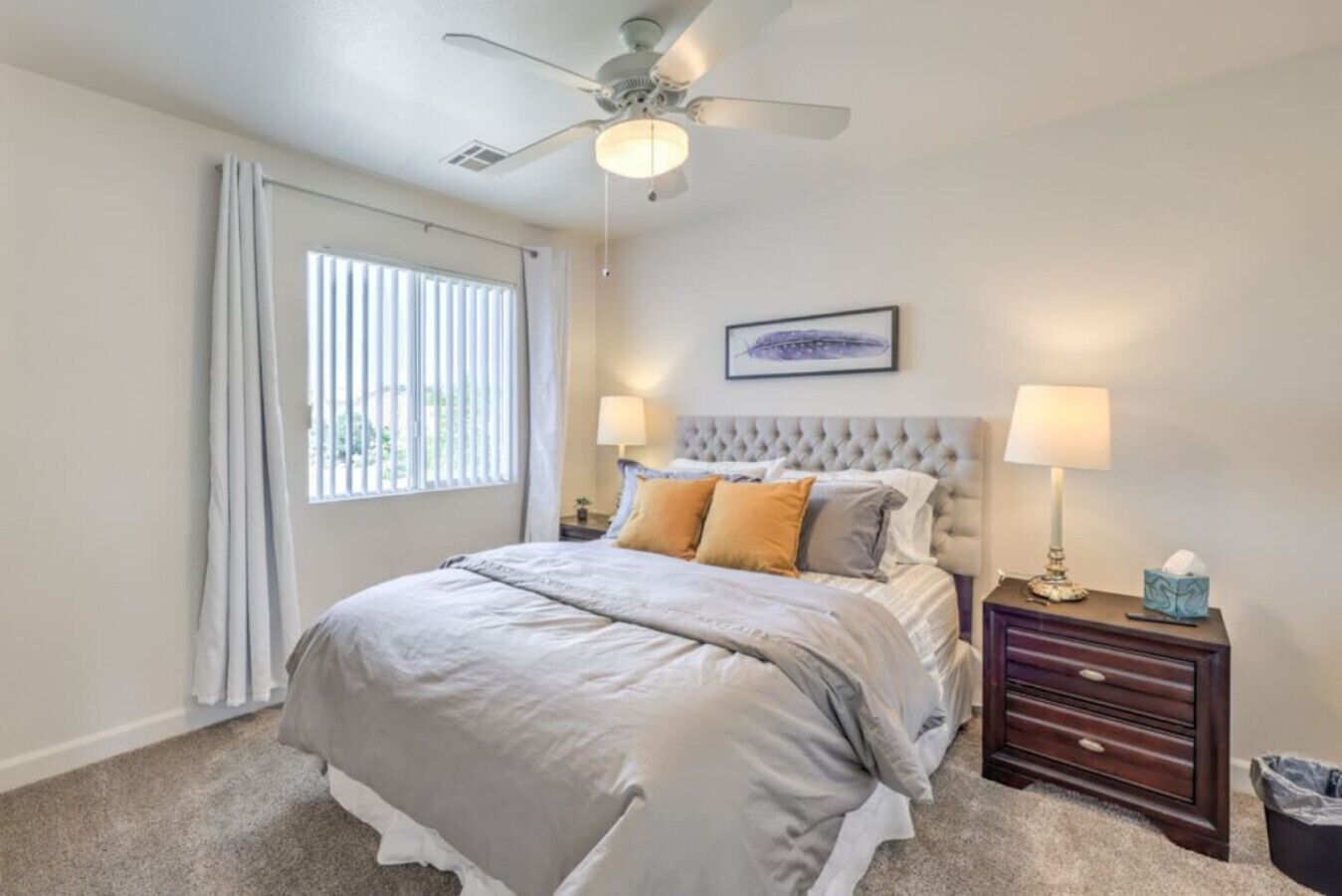 A bedroom with a bed, two bedside lamps, a nightstand, a ceiling fan, and a window with blinds.
