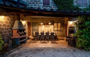 Une terrasse extérieure dotée d’une cheminée en pierre, de meubles en osier et d’un mur en pierre rustique.