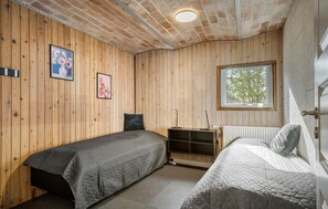 Une pièce aux murs en bois, avec deux lits, un radiateur, une fenêtre donnant sur un beau paysage et des tableaux encadrés accrochés au mur.