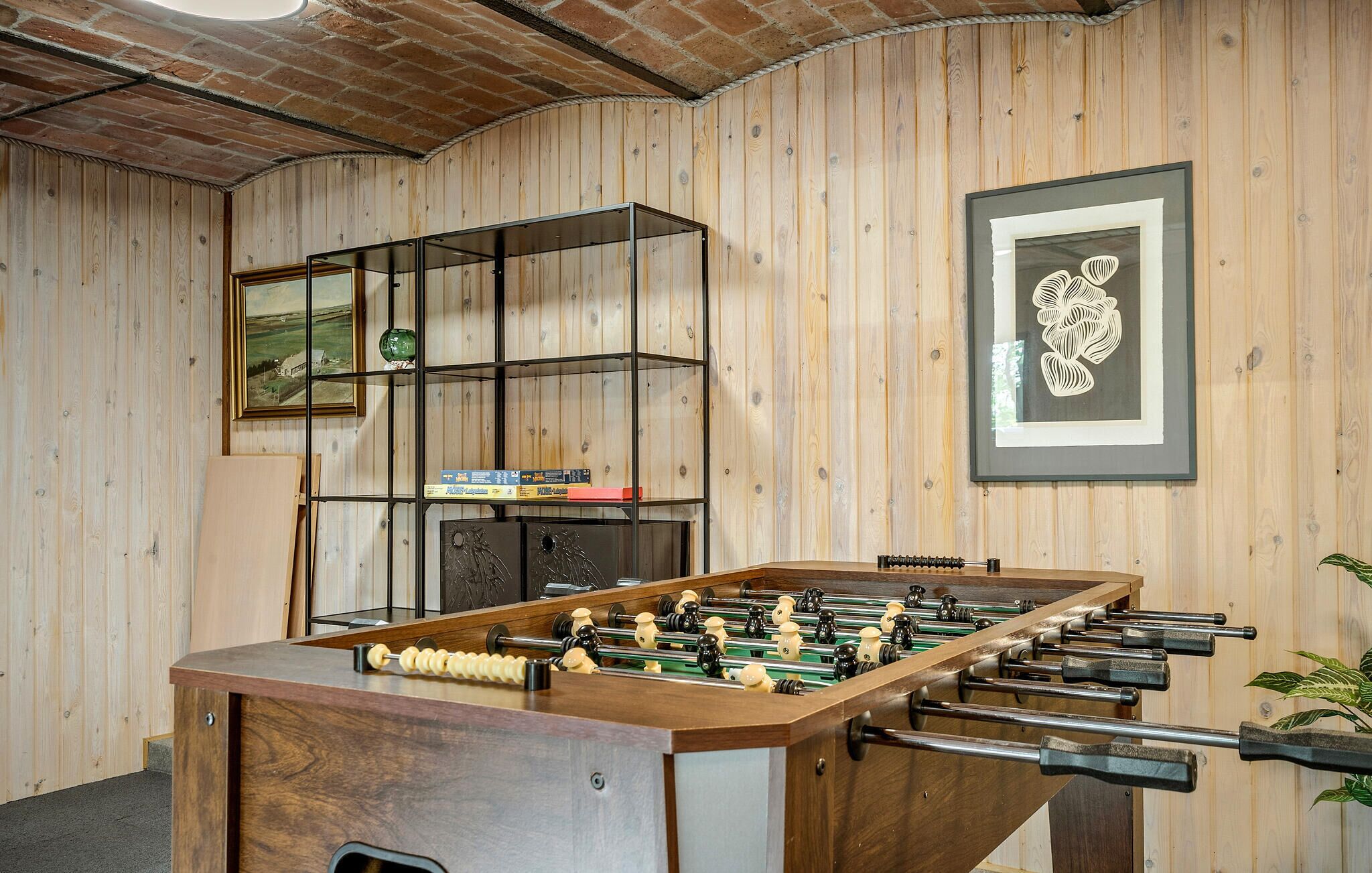 A room with a foosball table, a bookshelf, and framed artwork on the walls.