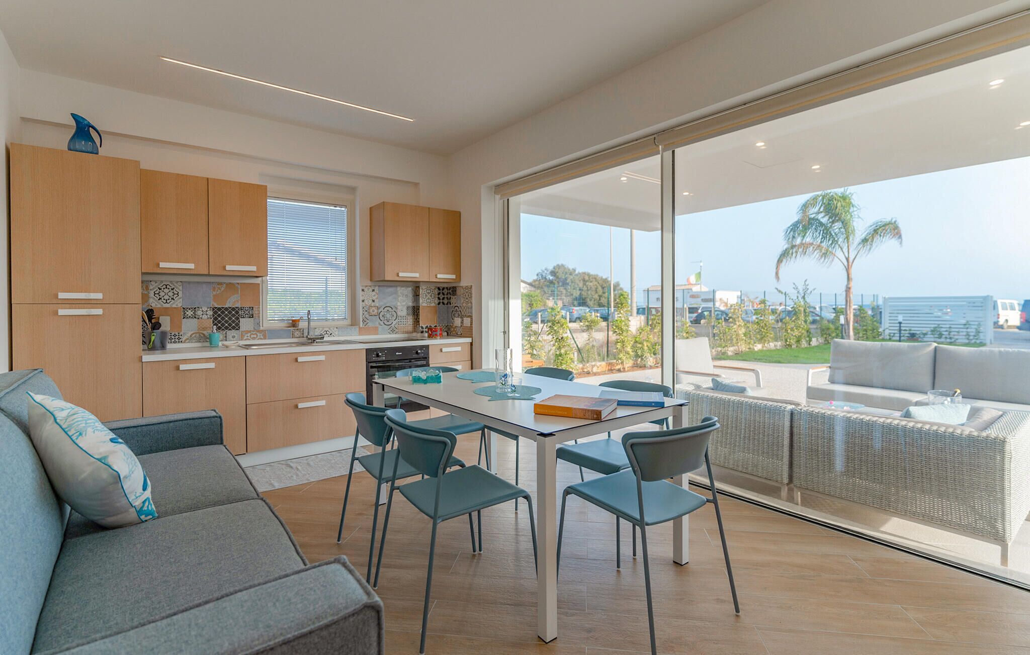 Une cuisine moderne avec des meubles en bois, un coin repas avec une table et des chaises, et un balcon avec vue sur la mer.