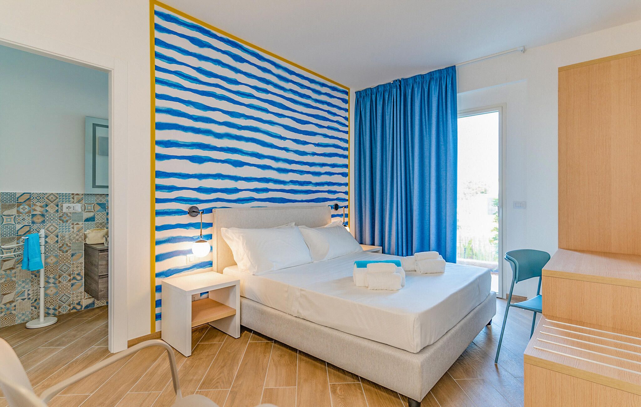 Quarto de hotel com uma cama, mesa de cabeceira, escrivaninha e uma cadeira.