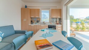 A modern kitchen with wooden cabinets, a dining area with a white table, and a view of the outdoors.