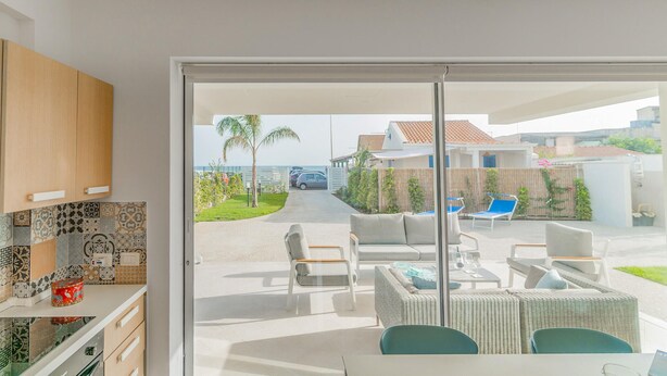 A modern kitchen with patterned tiles and wooden cabinets, leading to a patio with outdoor furniture and a view of a residential area.