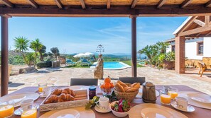A breakfast setup with croissants, orange juice, and coffee on a table overlooking a pool and mountains. - Los Menhires Villanueva de la Concepción by Ruralidays (Málaga)