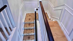 Una escalera con barandilla de madera, paredes blancas y un candelabro.