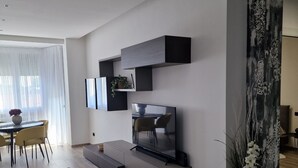 Ein modernes Wohnzimmer mit Flachbildfernseher, Einbauschränken und einem Essbereich mit gelben Stühlen.