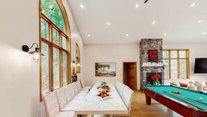 A dining area with a long table and benches, a pool table, and a stone fireplace. - 5 BR Luxury Escape with Hot Tub, Home Theater, Arcade, Min from Lake & Slopes (Tafton)
