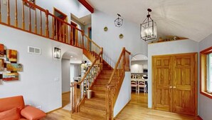 A spacious living area with a wooden staircase, a red sofa, and a wooden door. - 5 BR Luxury Escape with Hot Tub, Home Theater, Arcade, Min from Lake & Slopes (Tafton)