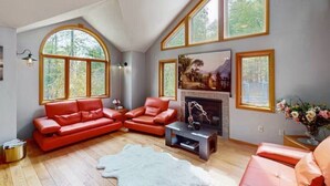 A spacious living room with a fireplace, large windows, and a modern red sofa set. - 5 BR Luxury Escape with Hot Tub, Home Theater, Arcade, Min from Lake & Slopes (Tafton)
