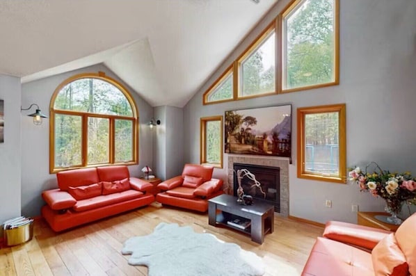 A spacious living room with a fireplace, large windows, and a modern red sofa set.