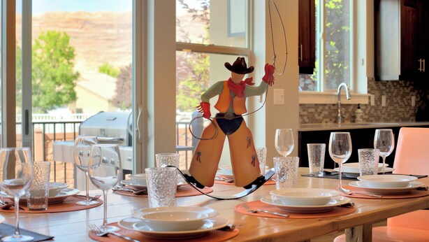 Une table à manger dressée avec des assiettes, des verres et des couverts, et une figurine de cowboy en arrière-plan.