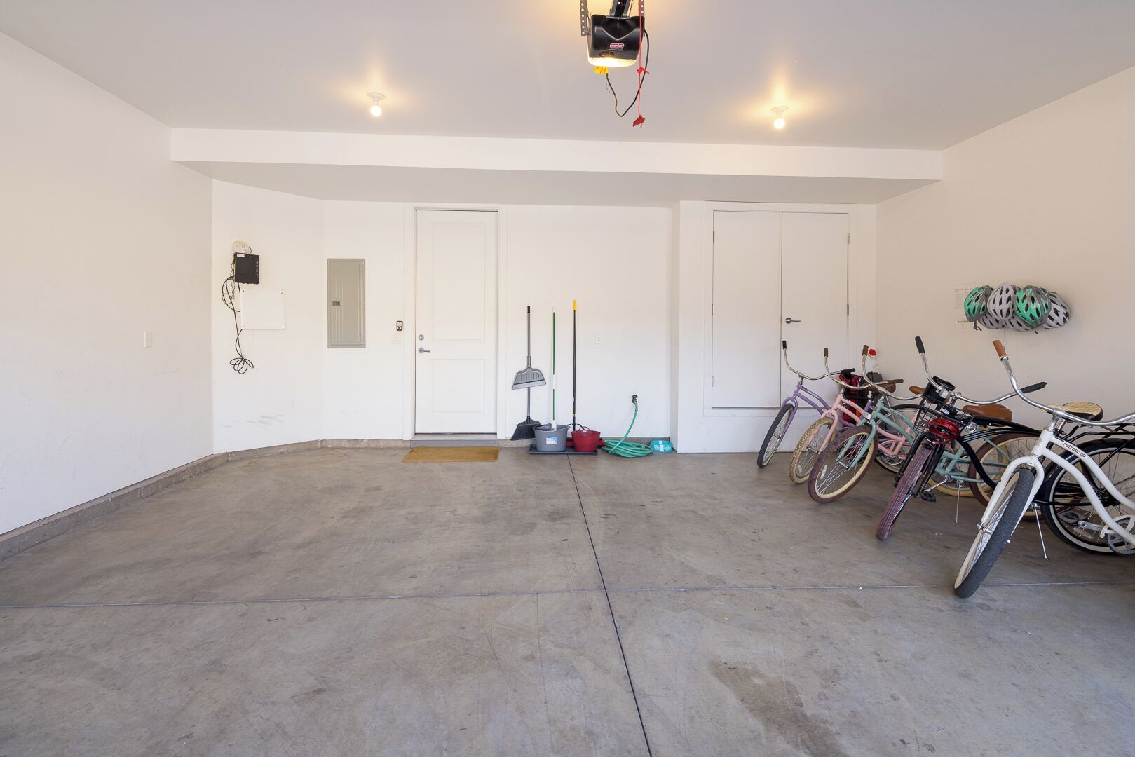 A spacious garage with concrete flooring, a white door, and several bicycles parked inside.