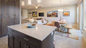 Une cuisine moderne avec des meubles en bois foncé, un îlot central, des luminaires suspendus et un coin repas avec une table dressée pour quatre personnes.