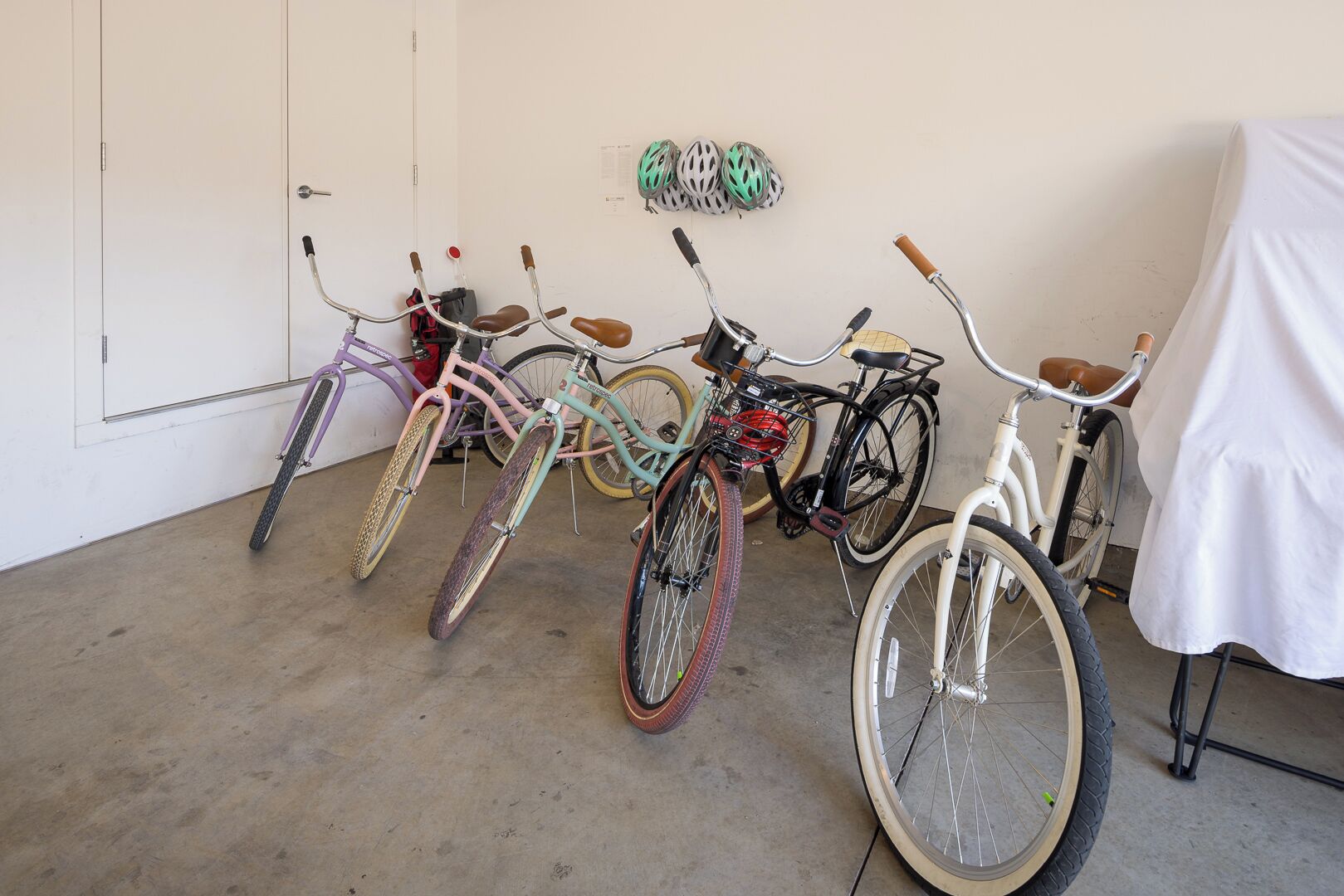 A row of bicycles parked indoors with a white door and a white wall in the background.