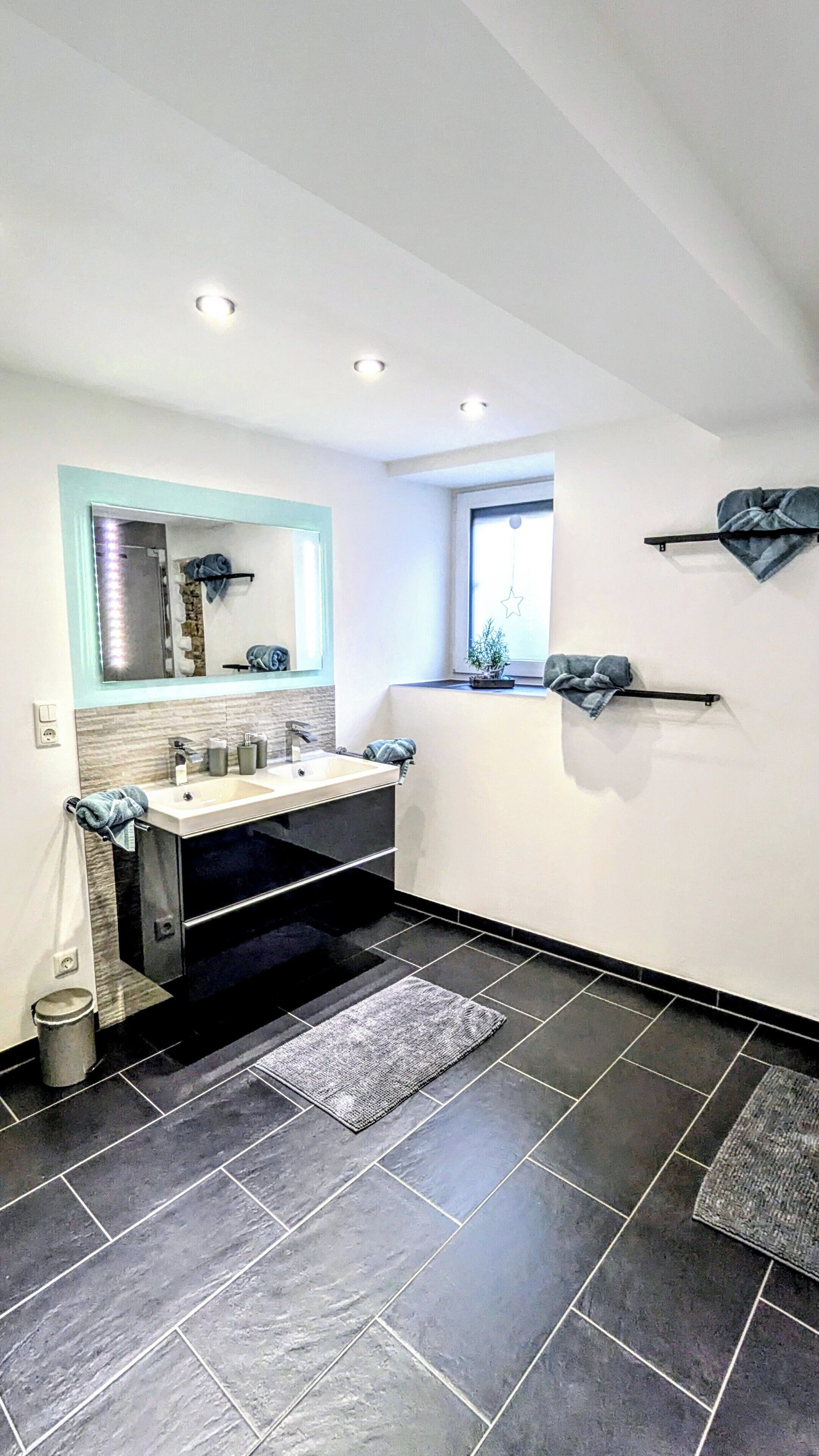 A modern bathroom with a large mirror, a sink, and a window.