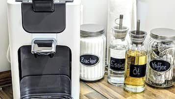A coffee machine with a black and white design, a roll of paper towels, and three labeled glass jars containing coffee-related items.