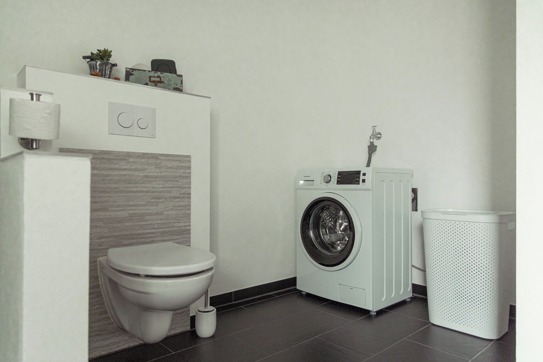 Ein kleines Badezimmer mit Toilette, Waschmaschine und Mülleimer.