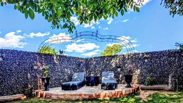 An outdoor seating area with a stone wall backdrop, a metal arch structure, and potted plants.
