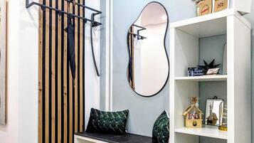 A modern room with a wooden floor, a bench with cushions, a mirror, and a white shelving unit with various items.