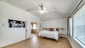 A spacious bedroom with a large bed, a ceiling fan, and a view of the outdoors through the window.