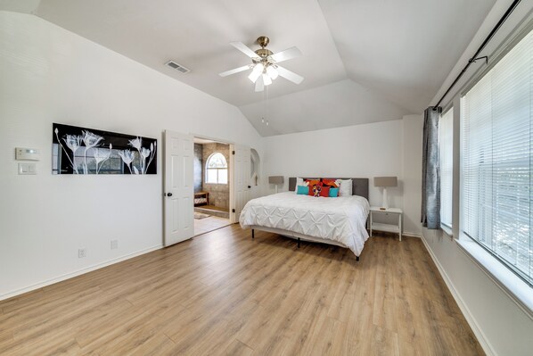 A spacious bedroom with a large bed, a ceiling fan, and a view of the outdoors through the window.