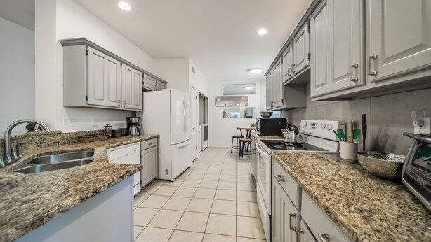 A modern kitchen with granite countertops, white cabinetry, and stainless steel appliances.