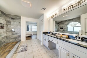 A modern bathroom with a large mirror, white cabinetry, and a stone accent wall.