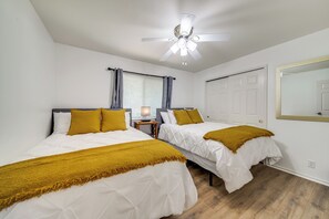 A bedroom with two beds, a ceiling fan, a nightstand with a lamp, and a window with curtains.