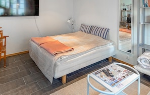 A modern bedroom with a bed, a bedside table with a remote control, a small table with magazines, and a mirror on the wall. - 1 bedroom cozy apartment in Brantevik (Brantevik)