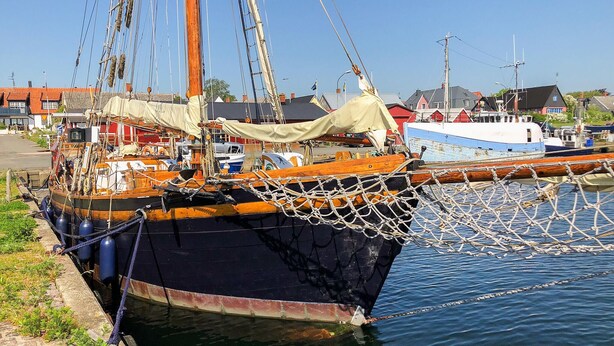 A docked sailboat with a netted bow, surrounded by other boats and buildings in a harbor.