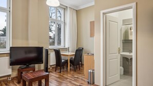 A modern living room with a flat-screen TV, wooden furniture, a dining area, and a view of trees through large windows. - Gorgeous apartment in Anklam (Anklam)
