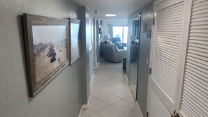 A hallway with a tiled floor, a framed picture on the left, and a door with a handle on the right. - SUNGLOW RESORT 503 Spacious Deluxe Ocean Front Corner Suite with Large Balcony (Daytona Beach Shores)