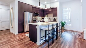 Une cuisine moderne avec des meubles de couleur bois foncé, des appareils en acier inoxydable et un îlot central doté de tabourets de bar.