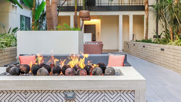 Un foyer extérieur entouré de pierres et un canapé, le tout agrémenté de plantes et avec un balcon en arrière-plan.