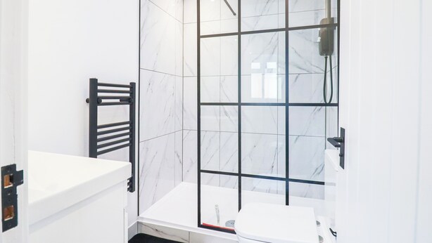 Un baño moderno con cabina de ducha de vidrio, un lavamanos blanco y un perchero negro.