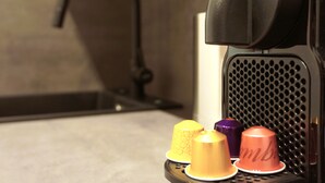A coffee machine with a black front panel and a perforated back panel.