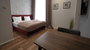A modern hotel room with a large bed, a wooden dining table, and two framed pictures on the wall.