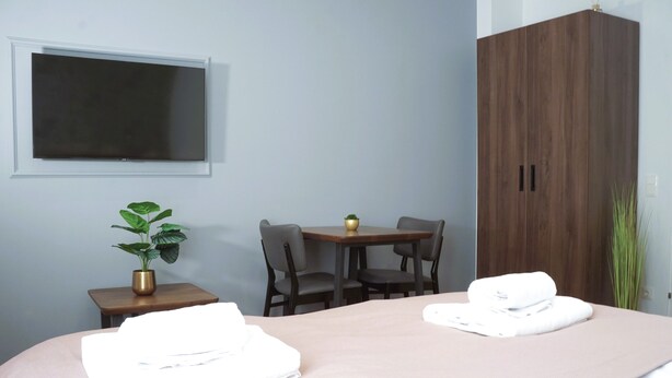 A hotel room with two beds, a TV mounted on the wall, a small table with chairs, and a wardrobe.