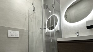 A modern bathroom with a glass-enclosed shower, a toilet, and a vanity with a mirror.