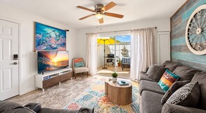 A living room with a ceiling fan, a television, a sofa, a coffee table, and a colorful rug.