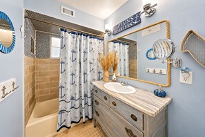 Un bagno a tema nautico con una vasca, un mobile bagno con specchio e un cartello che riporta la scritta 'CAPTAIN'S QUARTERS'.