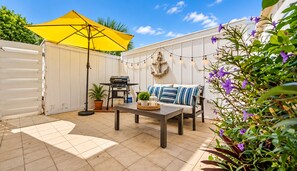 A patio area with a grill, outdoor furniture, and string lights.