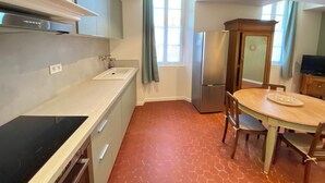 A kitchen with a black stove, a sink, cabinets, a refrigerator, a dining table with chairs, and a window with curtains.