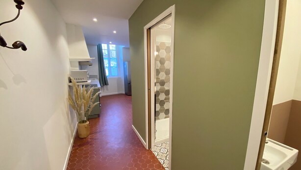 A hallway with a red-tiled floor, a white wall with a light switch, and a door with a geometric pattern.