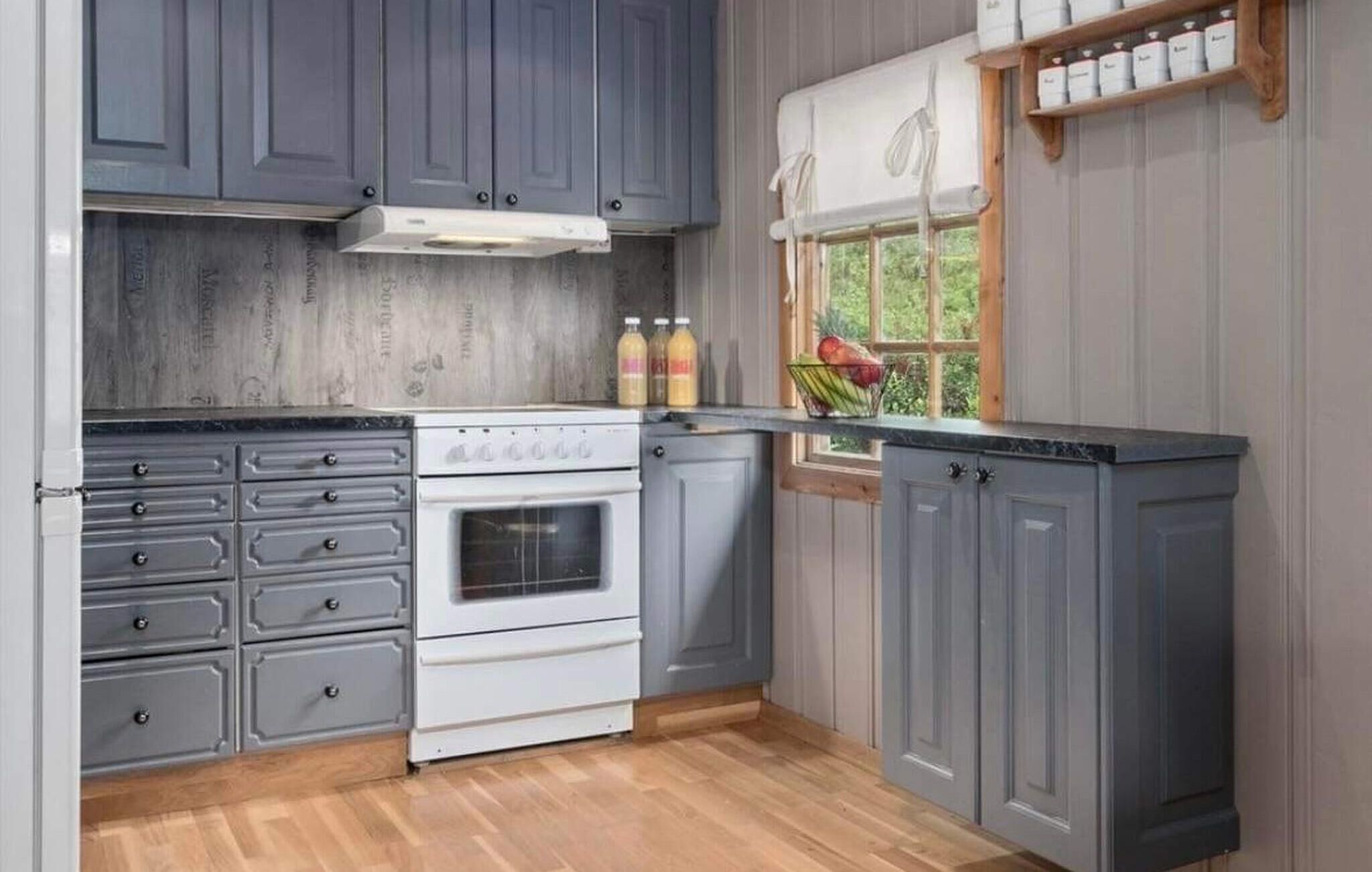 A kitchen with grey cabinets, a stove, and a window with a view of greenery.