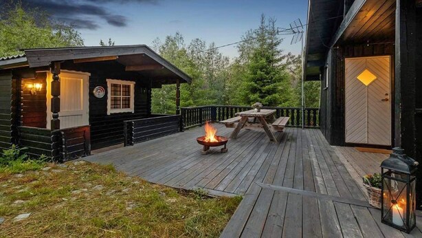 Een houten terras met een vuurkuil en een tafel, omringd door een houten blokhut met een veranda.